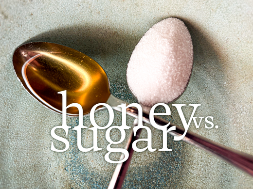 A spoon of honey compared to a spoon of sugar, crossed in an x above a hand made ceramic bowl. 